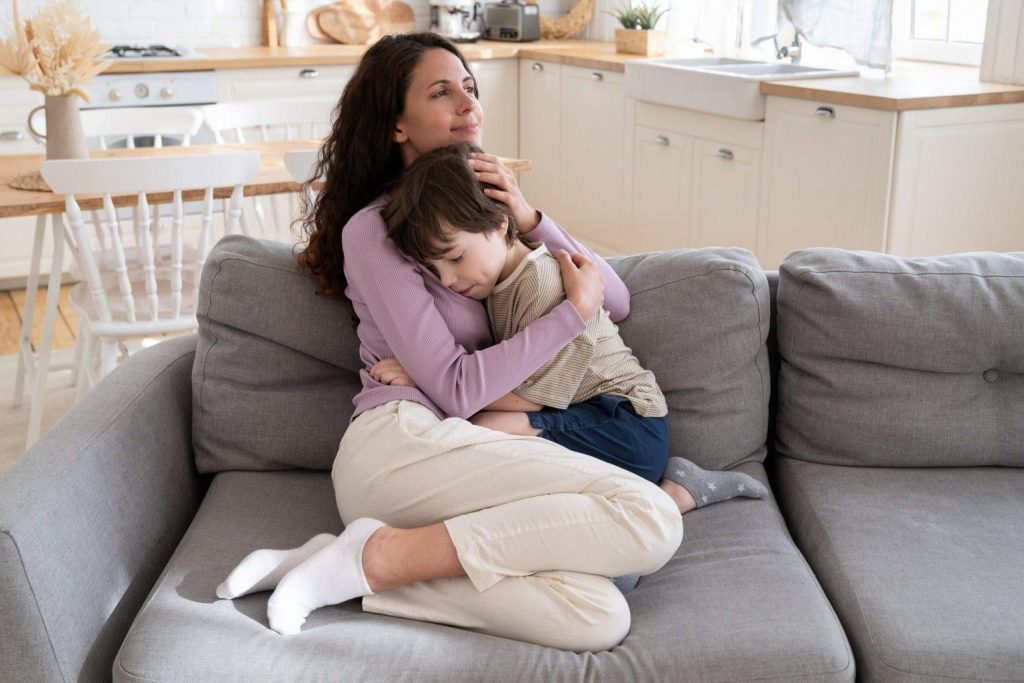 Mamă îmbrățișându-și copilul pe canapea, suport natural pentru reducerea anxietății în familie.