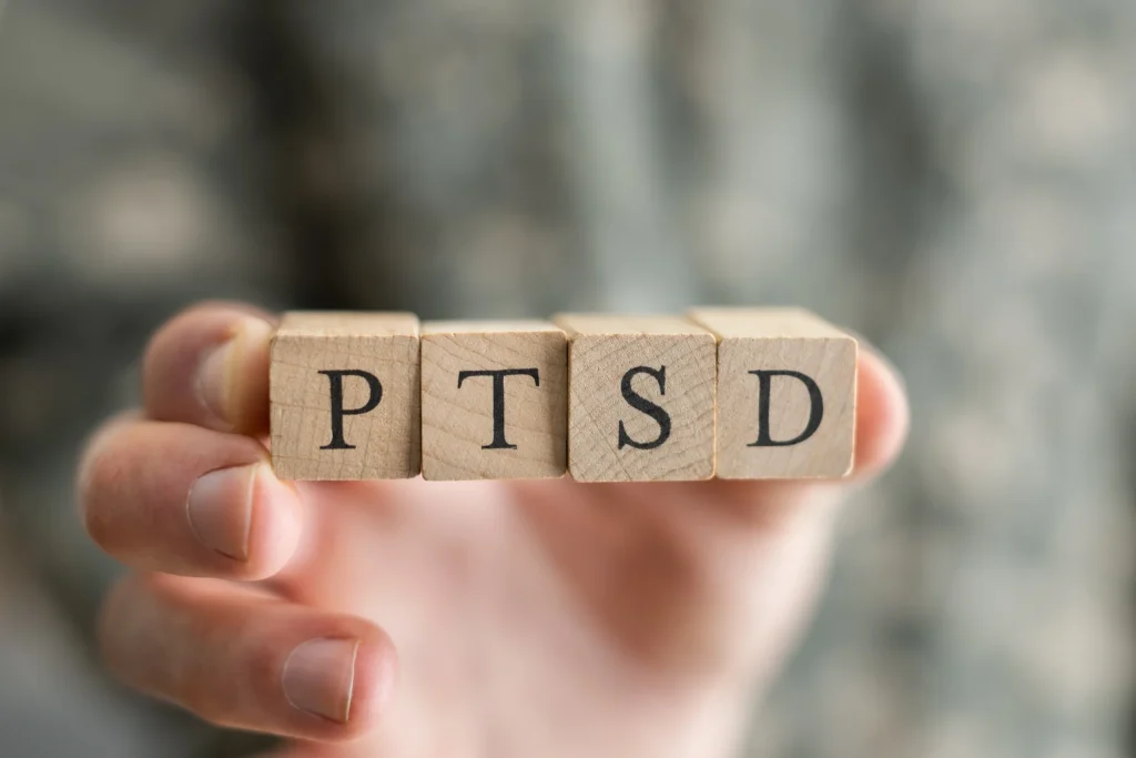Mână ținând cuburi din lemn pe care scrie PTSD, conștientizare și recuperare trauma.